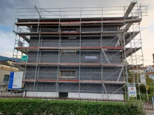 Gebäude vollständig von einem mehrstöckigen Baugerüst eingerahmt und Fassade ist mit dunklen Dämmplatten bedeckt