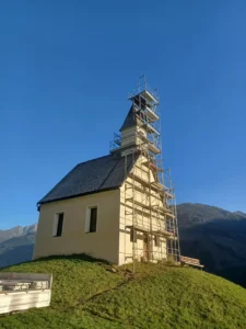 Kleine Kapelle auf einem Hügel, deren Eingangsseite und Glockenturm mit Gerüst eingerahmt sind