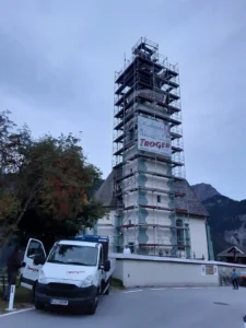 Kirchturm vollständig von einem hohen Gerüst umgeben, mit Werbeplanen der Gerüstfirma Troger